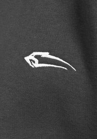 Tessuto grigio scuro con una fine trama a righe, caratterizzato da un logo ricamato bianco sul lato sinistro, modellato come una freccia astratta.