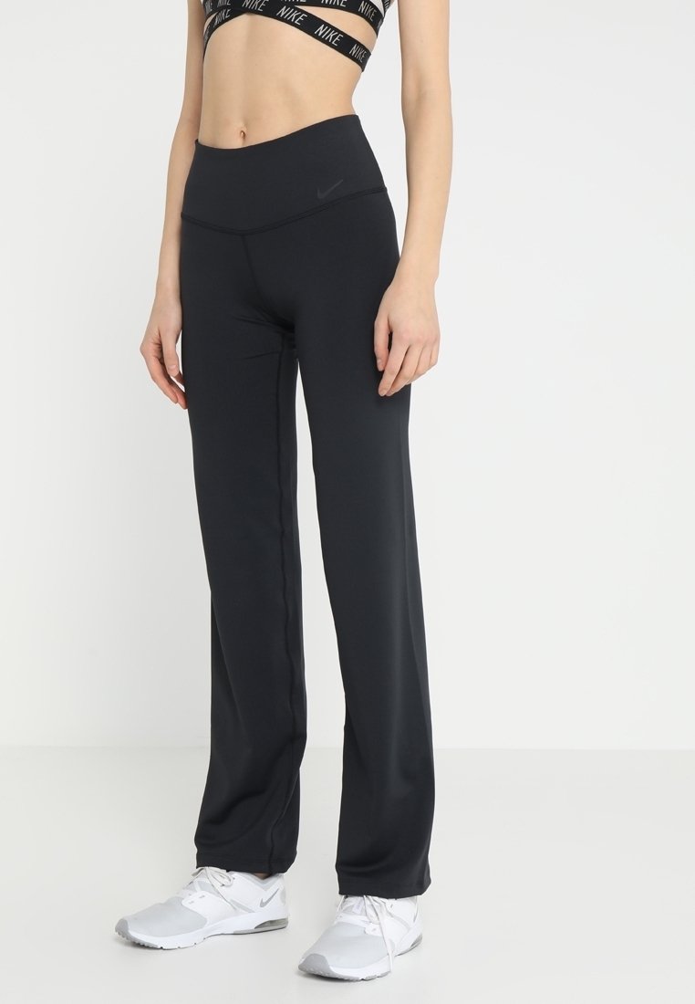 Schwarze Sporthosen aus dehnbarem Material mit hohem Bund und schmaler Passform, kombiniert mit weißen Sportschuhen.