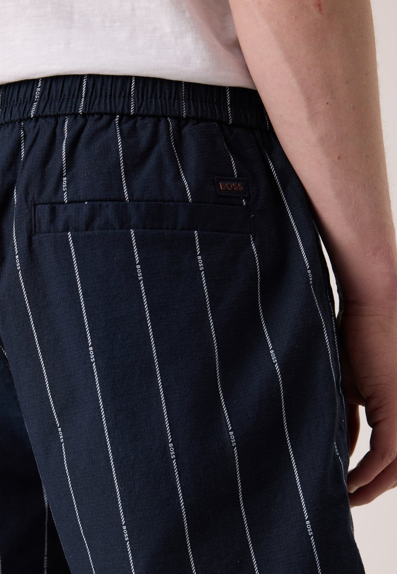 Marineblaue Hose mit elastischem Bund, die weiße vertikale Streifen und ein Logo-Patch an der hinteren Gesäßtasche aufweist. Weicher Stoff mit lässiger Passform.