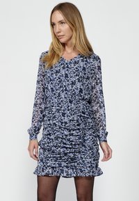 Kukallinen mekko sinisävyissä, jossa on v-pääntie, pitkät hihat, rypistyssä muotoilussa ja röyhelöhelma, valmistettu kevyestä kankaasta.