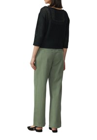 Zwarte gebreide trui met een losse pasvorm en 3/4 mouwen, gecombineerd met lichtgroene wijde broekspijpen. Eenvoudige zwarte flats maken de outfit compleet.