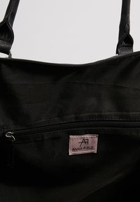 Sort nylon tote taske med sorte læderstropper. Har en lynlås i toppen og et pink mærke med "ANNA FIELD" indeni. Enkel og funktionel design.