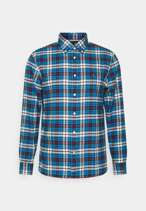 Chemise homme manches longues à boutons avec motif à carreaux bleu, blanc et marron et col boutonné, présentée sur un fond uni.