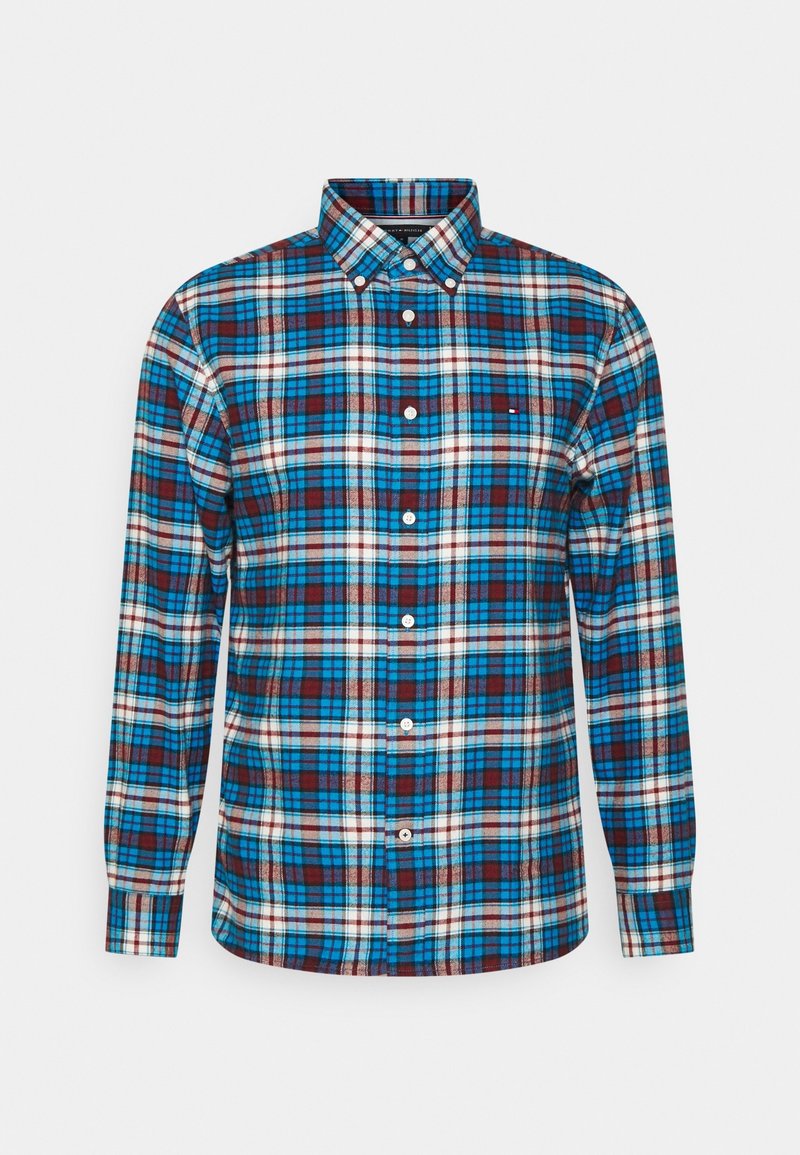 Chemise homme manches longues à boutons avec motif à carreaux bleu, blanc et marron et col boutonné, présentée sur un fond uni.