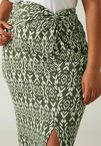 Gonna verde e bianca con motivo a fantasia, caratterizzata da un design frontale attorcigliato e da una spacco laterale. Realizzata in tessuto testurizzato con una superficie a coste.