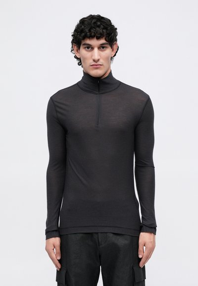 T-shirt noir à manches longues et col roulé avec fermeture éclair moitié; fabriqué à partir d'un tissu léger et lisse; design ajusté; porté avec un pantalon cargo texturé.