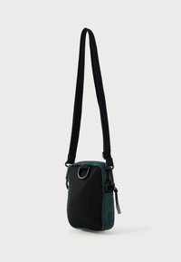 Grønn tverrkameraveske i stoff med svart netting foran, justerbar stropp og metallbeslag. Kompakt rektangulær form med glidelåslukking.