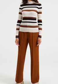 Maglione a coste con collo alto in bianco, marrone e nero abbinato a pantaloni larghi marroni. Calzature neutre texturizzate completano l'outfit.