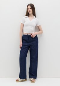 Witte cropped top met een textuurafwerking, gecombineerd met donkerblauwe wijde broek met een elastische tailleband en trekkoord. Beige plateausandalen.
