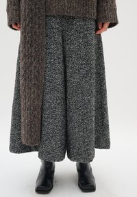 Brauner strukturierter Cardigan über einem weit geschnittenen Rock im schwarz-weißen Hahnentrittmuster, kombiniert mit schwarzen Stiefeletten.