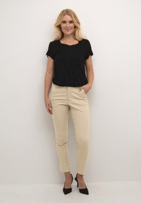 Black short-sleeve top with a square neckline, paired with beige slim-fit trousers and black high-heeled shoes.