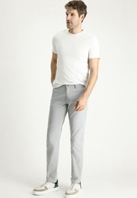Camiseta blanca de manga corta combinada con pantalones gris claro y zapatillas blancas con detalles en crema y verde. Corte entallado y textura suave.