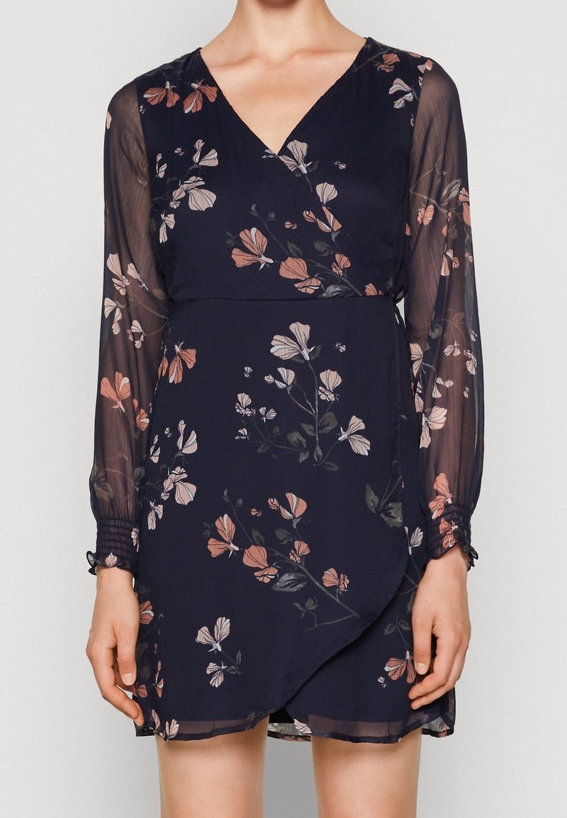 Robe portefeuille bleu marine avec manches longues transparentes, avec un motif floral en tons roses et blancs.
