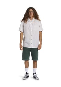 Kortærmet, hvid skjorte med vertikale, flerfarvede striber, lomme på venstre bryst, kombineret med grønne denimshorts og sorte sneakers.