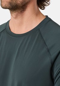 Donkergroen sportshirt met een ronde halslijn, lichte stof en subtiele perforaties. Bevat raglanmouwen en vlakke naden.