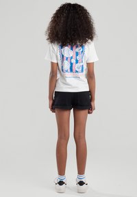 White short-sleeve t-shirt featuring a colorful shell graphic and text on the back, paired with black denim shorts. Sneakers with blue accents.