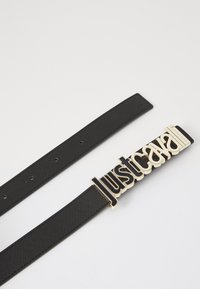 Zwarte stoffen riem met een grote gouden metalen gesp waarop de tekst "justcavalli" staat. De riem heeft meerdere gaatjes voor verstelbaarheid.