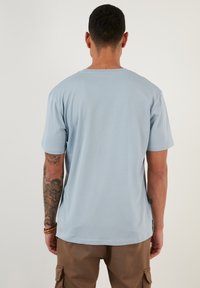Tricou scurt cu mânecă, de culoare albastru deschis, din material 100% bumbac, cu gât rotund, croială lejeră, textură netedă, design simplu, detalii de cusătură vizibile.