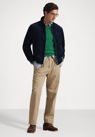 Casaco de panteão azul-marinho, suéter de malha verde, camisa às riscas, calças bege e sapatos castanhos. Apresenta um tecido texturizado e um corte casual.
