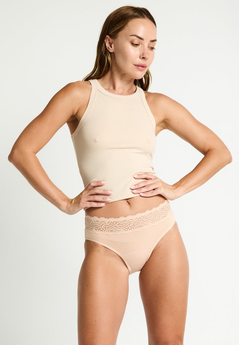 Débardeur beige en rib avec un col haut associé à une culotte beige avec des bordures en dentelle, présentant un détail de ceinture festonnée. Texture lisse.