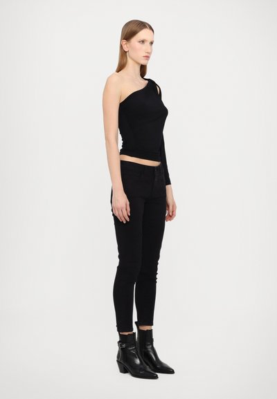 Svart én-skulder topp i myk tekstil, kombinert med tettsittende svarte jeans. Modellen har på seg svarte ankelstøvletter med liten hæl.