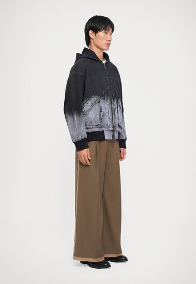 Black and grey gradient denim jacket with a hood, zip closure, and front pockets, paired with loose brown trousers and black footwear.