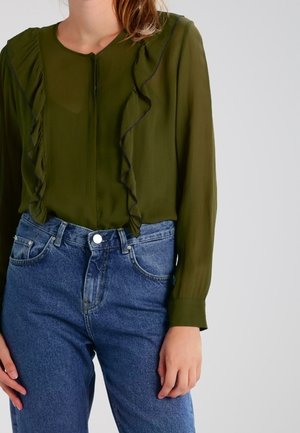 Olivengrøn bluse med rynkede detaljer langs fronten, parret med højhoftede blå denimjeans. Blusen har lange ærmer og knaplukning.