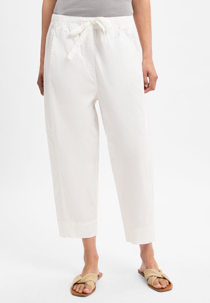 Weiße Baumwollhosen mit elastischem Bund und Kordelzug, mit lockerer Passform und verkürzter Länge. Getragen mit beigen flachen Sandalen.