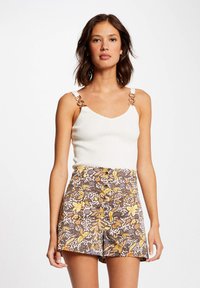 Débardeur blanc à côtelés avec des bretelles en cha�îne dorée, associé à un short marron avec des motifs floraux jaunes et des boutons à l'avant.