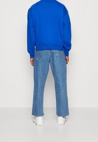 Modrá mikina s žebrovanými manžetami a lemem doplněná světle modrými rovnými džínami. Bílá teniska s texturovanými detaily dokončuje outfit.