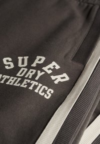 Donkergrijze sportshorts met witte "SUPER DRY ATHLETICS" opdruk, voorzien van een geribde tailleband en zijzakken.