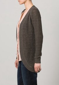 Graue Strickjacke mit entspannter Passform, offenem Vorderteil und gerippten Ärmeln, getragen über einem hellrosa Oberteil mit strukturiertem Finish.