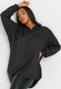 Camicia nera con bottoni, a pois bianchi, maniche lunghe e orlo curvo. Realizzata in un tessuto testurizzato con una vestibilità comoda.