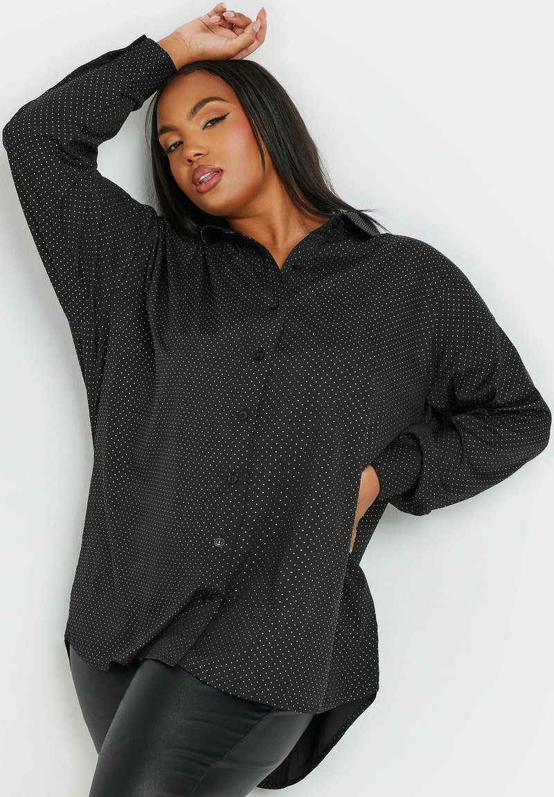 Camicia nera con bottoni, a pois bianchi, maniche lunghe e orlo curvo. Realizzata in un tessuto testurizzato con una vestibilità comoda.