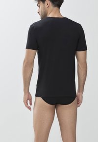 T-shirt nero a maniche corte con collo rotondo, realizzato in tessuto morbido, mostrato da dietro su un modello che indossa biancheria intima nera abbinata.