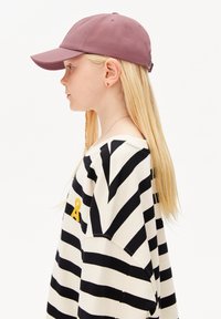 Bordeauxfarbene Baseballmütze mit einem strukturierten Schirm, getragen mit einem schwarz-weißen gestreiften Pullover, der ein kleines gelbes Detail auf der Brust hat.