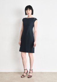 Navy blue sleeveless dress with a fitted silhouette, featuring sheer shoulder cutouts and a smooth texture. Paired with black strappy heels.