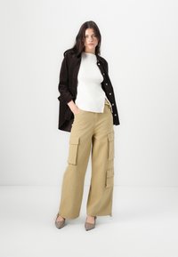 Beige cargo pants with large pockets paired with a white ribbed top and dark brown corduroy shirt. Light brown pointed toe heels.