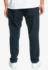 Pantalons en coton bleu marine avec une coupe décontractée, dotés de poignets roulés et d'une texture lisse, associés à des baskets blanches.