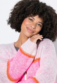 Rosa und weiße Strickjacke mit orangen Streifen, die eine weiche Textur und eine lockere Passform aufweist. Offenes Vorderdesign mit langen Ärmeln.