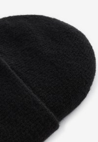 Schwarze, gestrickte Mütze mit weichem, strukturiertem Finish. Die runde Form verfügt über einen umgeschlagenen Rand für zusätzlichen Wärmeschutz und vielseitigen Stil.