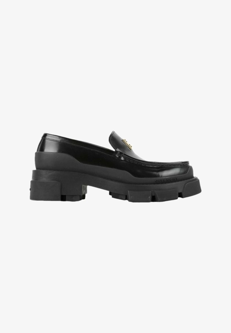 Mocassin en cuir noir avec semelle épaisse en caoutchouc et logo métallique doré sur le dessus, vue de côté sur fond blanc.