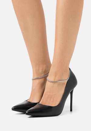 Escarpins en cuir verni noir avec bouts pointus et talon stiletto. Dotés d'une bride cheville en chaîne argentée pour plus de détail.