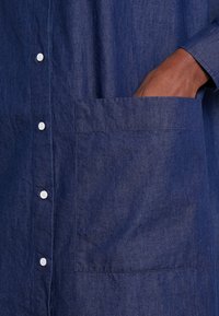 Marinblå knappar upp skjorta med en bröstficka, tillverkad av ett texturerat tyg med synliga sömmar och vita knappar.