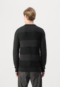 Maglione nero a maglia con strisce orizzontali grigie, lavorazione a coste e maniche lunghe. Collo rotondo e polsini aderenti. Inquadratura della vista posteriore.