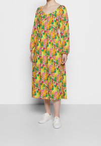 Blommig maxiklänning med rundad halsringning, långa puffärmar och livfulla färger inklusive gul, rosa, grön och orange. Slät tyg.