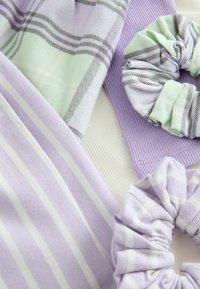 Violetti ja vihreät saksit, joissa on erilaisia tekstuureja; yhdessä on raidallinen kuvio, toisessa ruudullinen muotoilu. Pehmeä, joustava kangas.