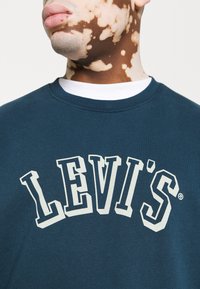Modrá bavlněná mikina s velkým bílým logem "LEVI'S" vytištěným na hrudi, kulatým výstřihem a žebrovanými manžetami.
