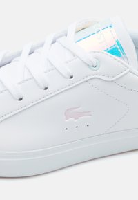 Baltos odinės sportinės bateliai su lygiomis raišteliais, su rožiniu iškilniu logotipu, perforacijomis vėdinimui ir blizgesiu mėlynai akcentuota liežuvėliu.