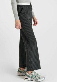 Pantalons larges à rayures noires avec une taille élastique et un cordon de serrage, associés à un pull en maille grise texturée et des chaussures de sport à motifs.
